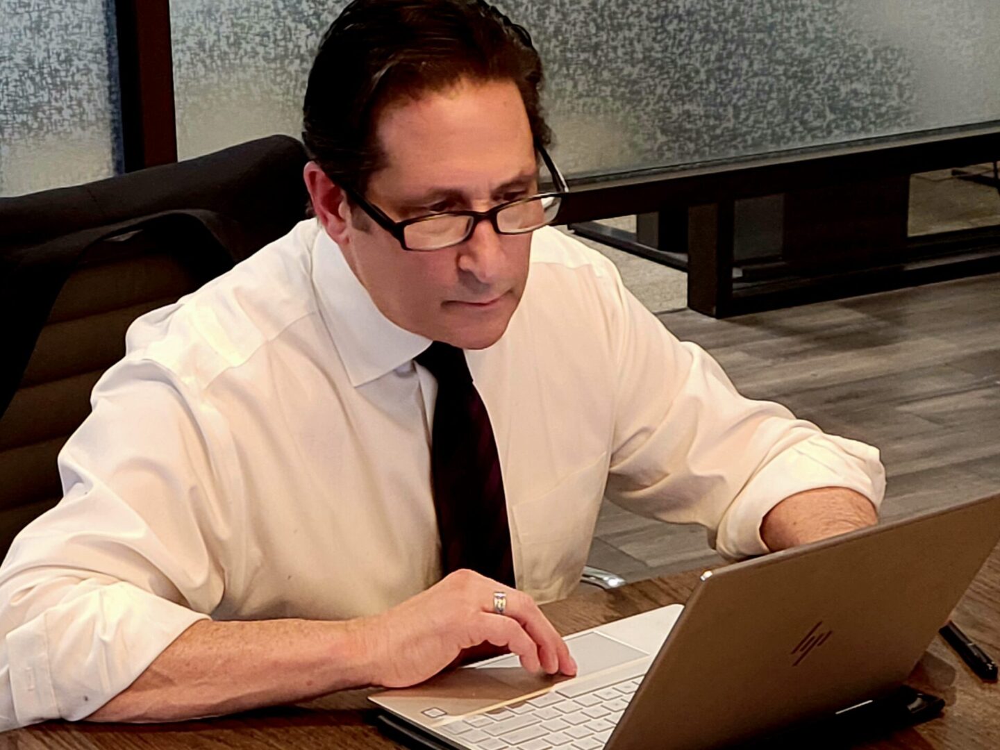 A man in glasses and a tie is on his laptop